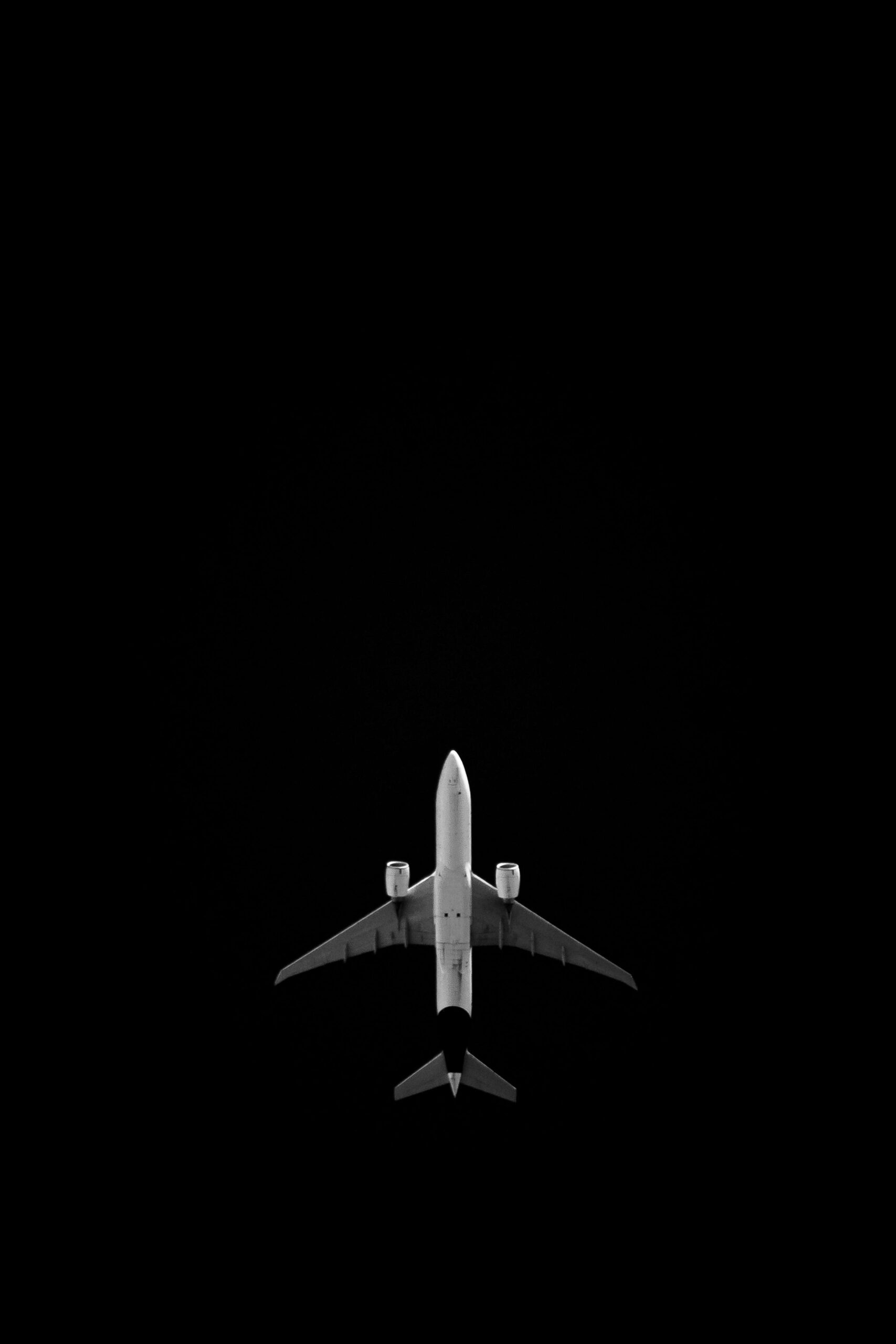 A sleek airplane captured flying directly below against a dark night sky.